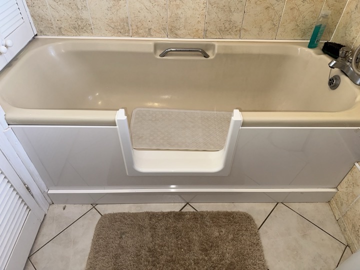 The open step-in frame fitted into a customer's older bath, with a bath mat in the tub